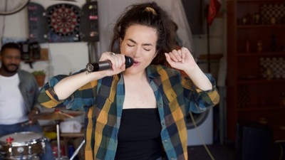 Action shot of Alma Cook singing with a garage band in the "5000 Candles" music video