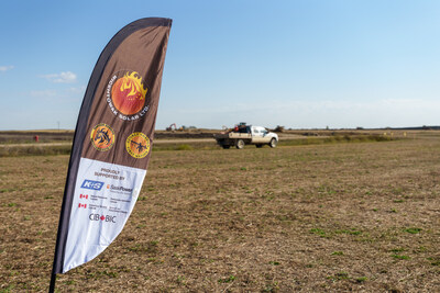 A feather flag for Wicehtowak Solar Ltd., mentioning the partnership with the CIB and other organizations, stands in the foreground of a dry, open field with a white pickup truck and construction equipment visible in the distance under a clear blue sky. (CNW Group/Canada Infrastructure Bank)